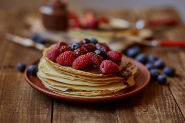 Homemade crepes, tasty thin pancakes with chocolate and fruits on the rustic table