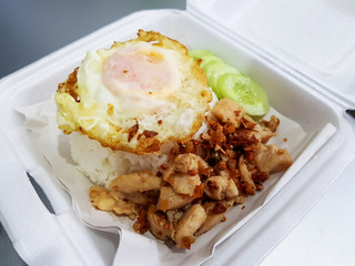 Garlic fried chicken topped with rice and a fried egg on paper for serving food in a foam box
