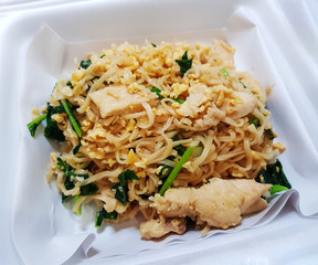 Stir-fried instant noodles with chicken and egg on paper for serving food in a foam box