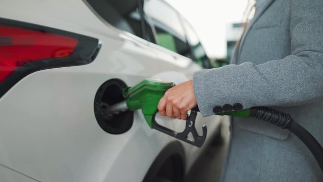 Woman fills petrol into her car at a gas station. Slow motion