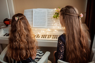 Fototapeta premium Home piano lesson. Two girls play the piano together. Family concept. The idea of activities for children during quarantine.