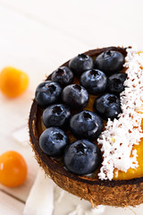 smoothie bowl with blueberries, frozen mango puree and coconut shavings in coconut bowl on white background