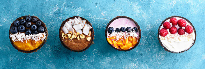 top view four colorful smoothie bowls with blueberries, raspberries, physalis and coconut shavings...