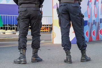 The back view of police officers wearing black uniform patrolling streets with walkie-talkie. Security city guards in outfit controlling entrance. Policemen trousers and boots of modern design.