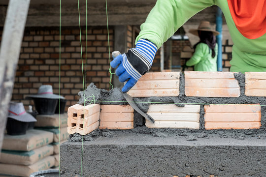 Close up of mansory bricklayer worker hand installing bricks on construction site
