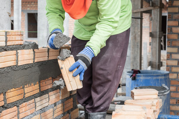 Close up of mansory bricklayer worker hand installing bricks on construction site