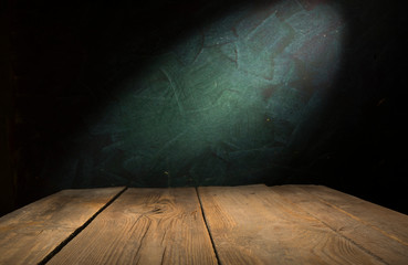 Old wood table with blurred concrete block wall in dark room background.