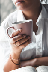 Woman in a white t-shirt holds morning coffee in a pink ceramic cup. Manicure. Front view