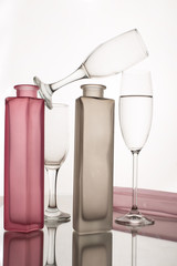 Colored still life consisting of three glasses and tree bottles on a monochromatic white background