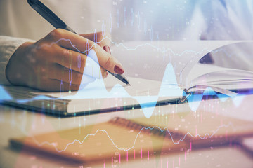 Multi exposure of woman's hands making notes with forex graph hologram. Concept stock market...