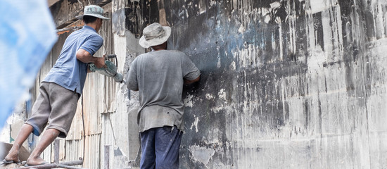 Thai construction labor worker is using jackhammer in destroy or destruction old building at construction site.