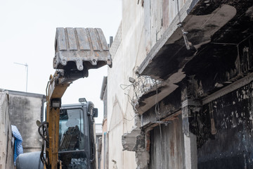 Small yellow excavator is on duty for pulling down the old buildings. Selective focus at bucket.