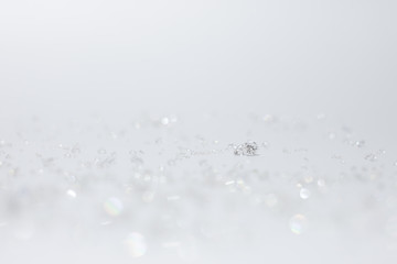 Round brilliant cut diamond in front of a white background, glitter lights bokeh abstract wallpaper, reflections on the ground. copy space and effect lighting for design.