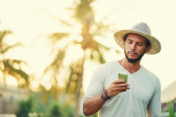 Obraz premium Vacation and technology. Young man using smartphone on tropical resort.