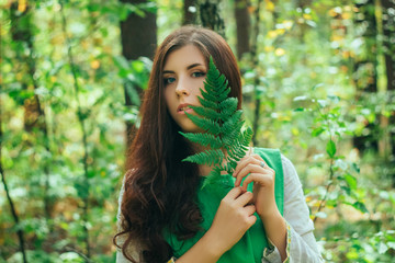 A young, attractive woman in a green dress from a medieval villager holds a fern leaf in her hands....