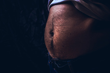 Close up of perfect male body with a belly or paunch isolated on black background with copy space.
