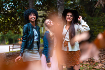Lifestyle session. Three good friends in an autumn session under a tree with falling leaves, a blonde, a brunette and a Latin girl with afro hair
