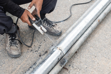 A welder with no protective mask and gloves is welding steel pipes with electrode at outdoor space.