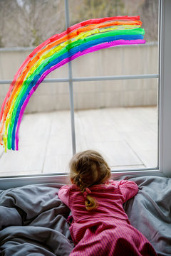 Adoralbe Little Toddler Girl With Rainbow Painted With Colorful Window Color During Pandemic Coronavirus Quarantine. Child Painting Rainbows Around The World With The Words Let's All Be Well.