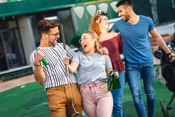 Group of smiling friends going to play mini golf in the city.	