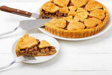 Closeup homemade apple pie with cinnamon and walnut on white wooden table. Shallow focus.