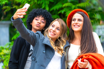 Street style session. Three smiling friends making a selfie in the city, a blonde, a brunette and a Latin girl with afro hair