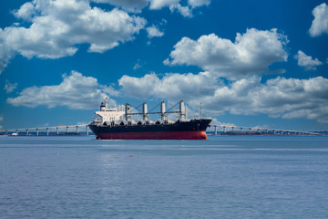 A huge old freighter on calm water by a white bridge