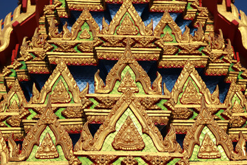 Close up detail of the ornate decoration on a Buddhist Thai temple roof with rows of small Buddha icon designs in gold