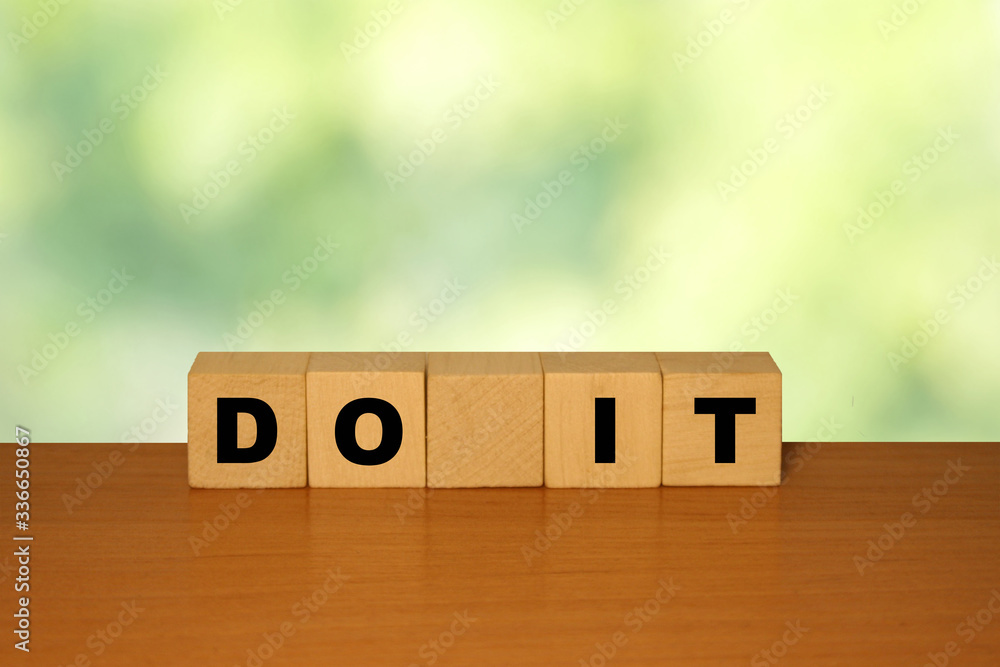 Poster do it message word on a wooden desk on cube blocks with a green nature background.
