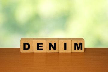 DENIM message word on a wooden desk on cube blocks with a green nature background.