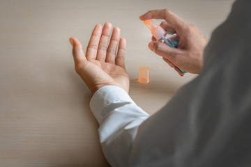 Closeup man using alcohol spray to clean hands on desk. Coronavirus diseases prevention concept.