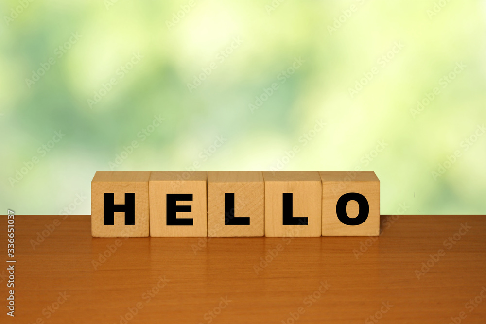 Poster hello message word on a wooden desk on cube blocks with a green nature background.
