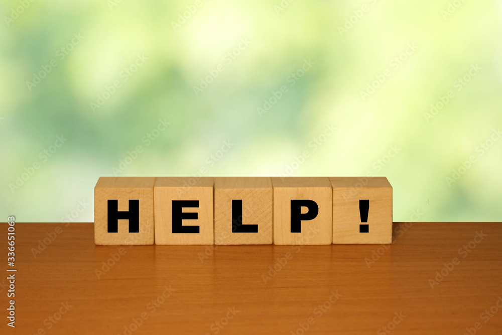 Poster help message word on a wooden desk on cube blocks with a green nature background.