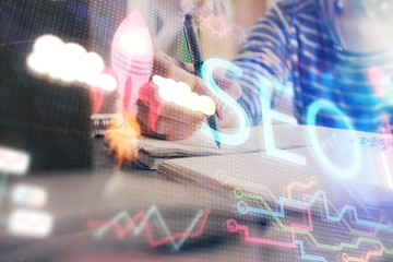 Multi exposure of woman's hands making notes with SEO icon. Concept of Search engine optimization