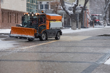 Fototapeta na wymiar Snow plow is sprincling salt or de-icing chemicals on pavement in city. Cleaning service. Frost winter season. Winter anti-slip road handling concept.