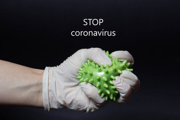 Hand in a medical glove tightly compresses a coronavirus on a black background. Close up