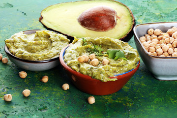 Bowl of green hummus, delicious cream of chickpeas and avocado with herbs on background
