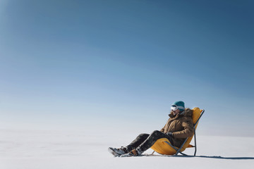 guy in a snowy field sitting on a yellow deck chair and looking forward