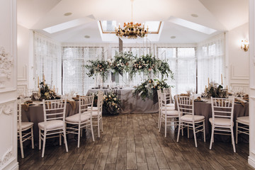 Wedding banquet. Celebratory tables with tablecloths are decorated with compositions of flowers, on the tables are plates with napkins, glasses and candles