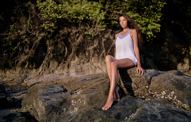 Outdoor portrait of beautiful young woman with long hair sitting on the rock.