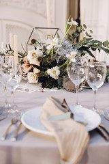 Wedding banquet. Celebratory tables with tablecloths are decorated with compositions of flowers, on the tables are plates with napkins, glasses and candles
