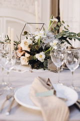 Wedding banquet. Celebratory tables with tablecloths are decorated with compositions of flowers, on the tables are plates with napkins, glasses and candles