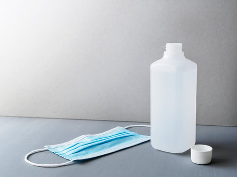 Desinfektionsmittel in einer Plastikflasche und eine blaue Schutzmaske auf einem grauen Tisch, Corona Virus, Pandemie, Schutzma&szlig;nahme