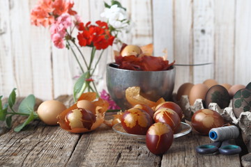 Easter background. Colored eggs in a glass plate with flowers on a wooden old background.