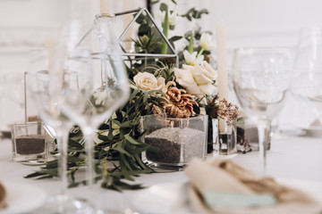 Wedding banquet. Celebratory tables with tablecloths are decorated with compositions of flowers, on the tables are plates with napkins, glasses and candles