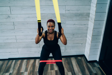Short haired smiling young African American woman squatting with resistance band and expander