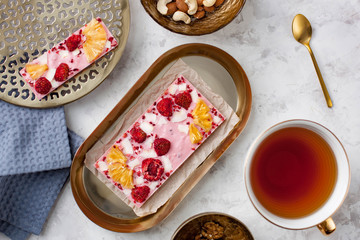 handmade pink chocolate bar with pineapple, strawberry and coconut lying on the table near a cup of tea