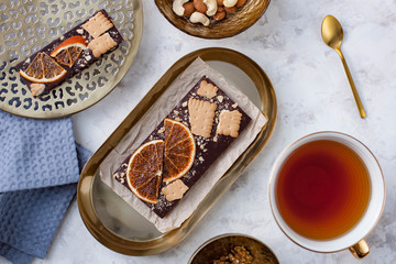 handmade chocolate bar with cookies and slices of dried oranges lying on the table near a cup of tea