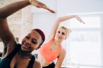 Diverse women stretching back and side muscles in fitness room
