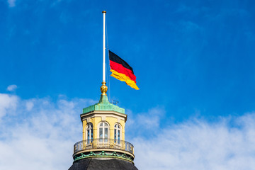 German Flag at Halfmast, auf Halbmast, on tower roof of Castle Karlsruhe. Blue sky in background....